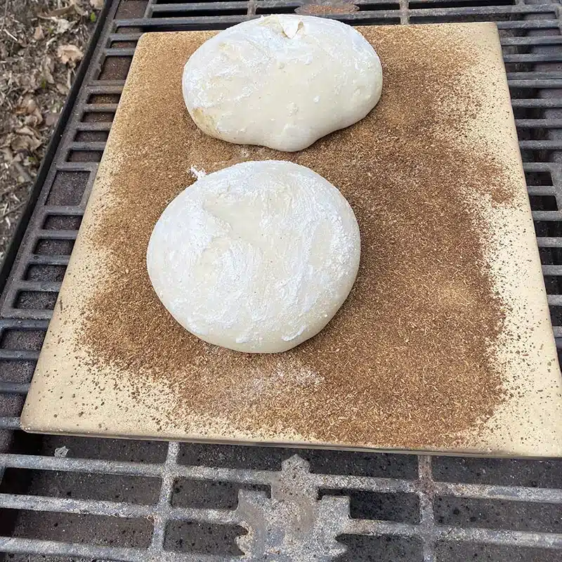 Bread dough on a pizza stone on a grill.